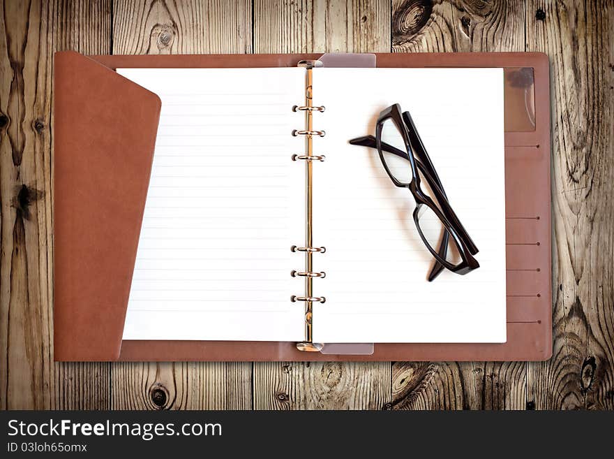 Eyeglasses on notebook isolated on wood texture