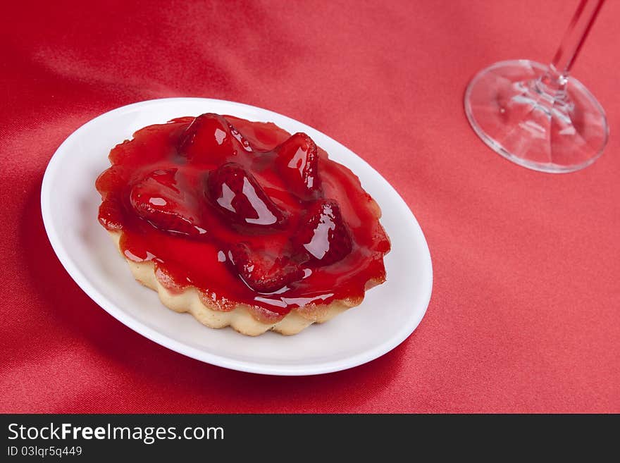 Strawberry cake topped with strawberry glaze on red satin background