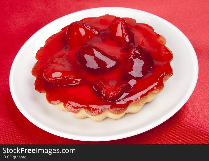 Strawberry cake topped with strawberry glaze on red satin background