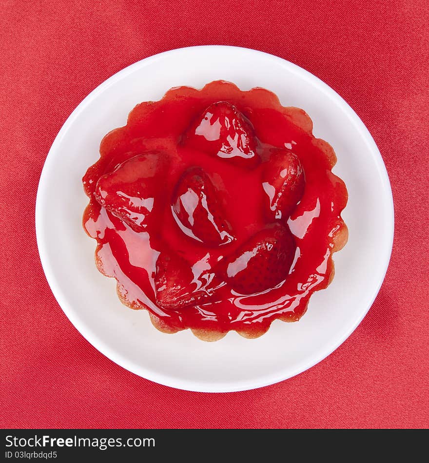 Strawberry cake topped with strawberry glaze on red satin background