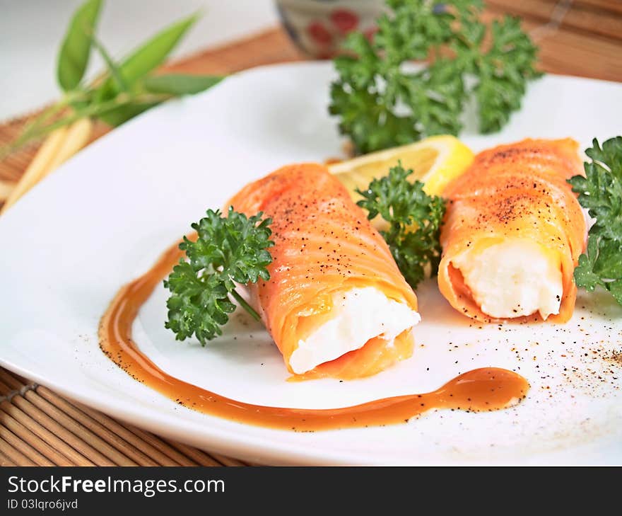 Salmon and cheese rolls with pepper, parseley and lemon on a white plate