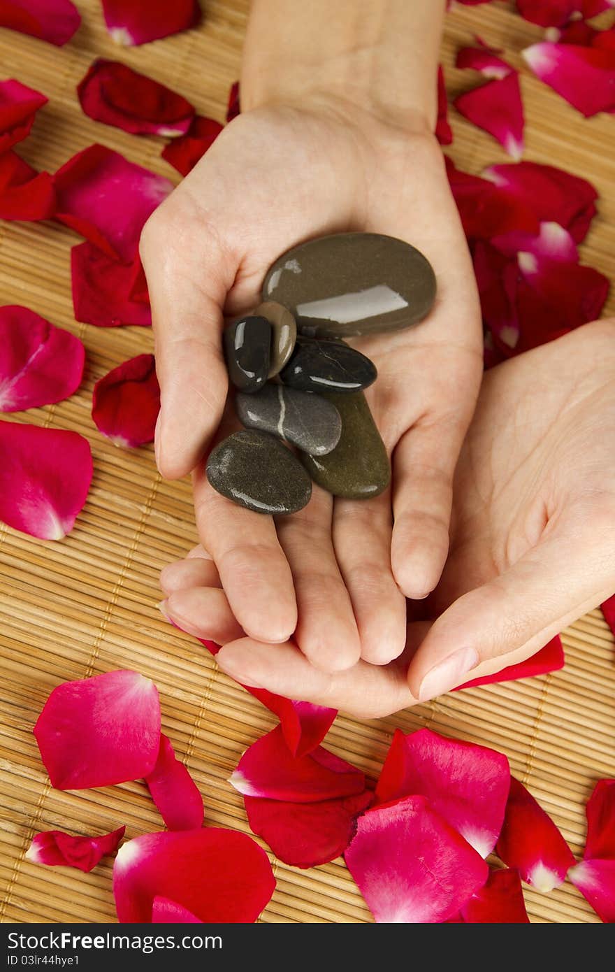 Close-up of beautiful girls hands are on red rose petals. In the hands of the stones are. Close-up of beautiful girls hands are on red rose petals. In the hands of the stones are