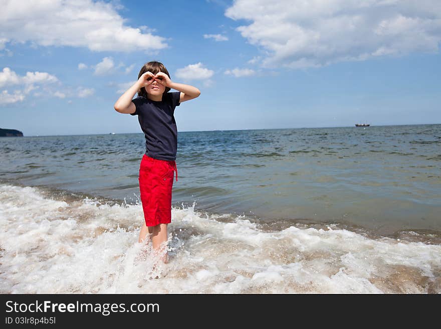 Boy standing in the sea, and pretends to hold in the hands of binoculars. Boy standing in the sea, and pretends to hold in the hands of binoculars