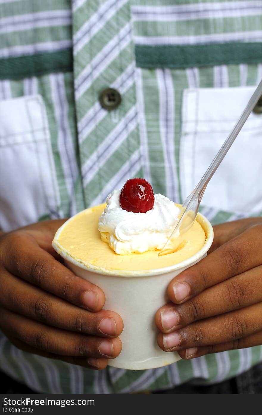 A child holding cup cake topped with cream and cherry. A child holding cup cake topped with cream and cherry