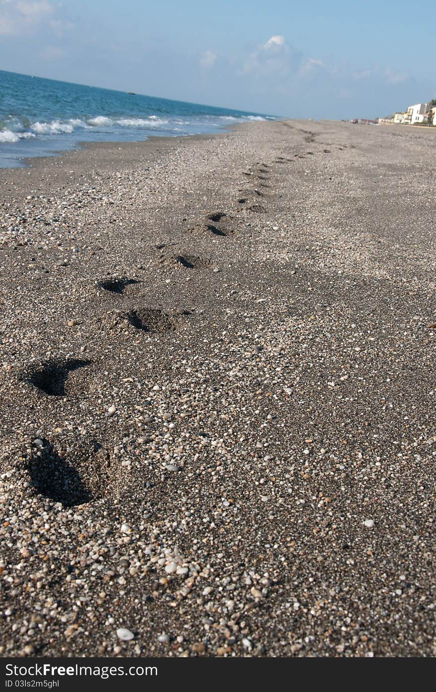 Footprints on the sand with waves crashing near