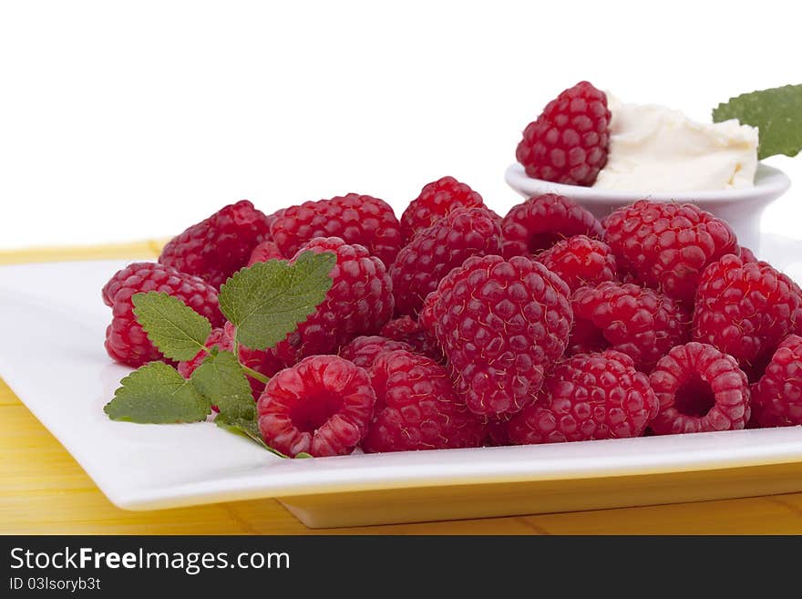 Studio-shot of a plate with raspberries garnished with lemon balm and a small bowl of sweet mascarpone, isolated on white.