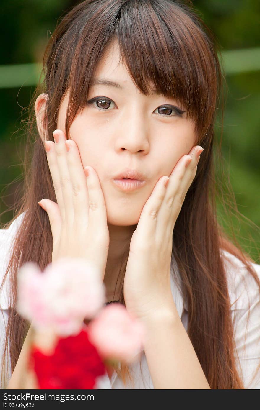 Young healthy Thai girl portrait in the park with flowers, focus at Model, hands on her cheek. Young healthy Thai girl portrait in the park with flowers, focus at Model, hands on her cheek