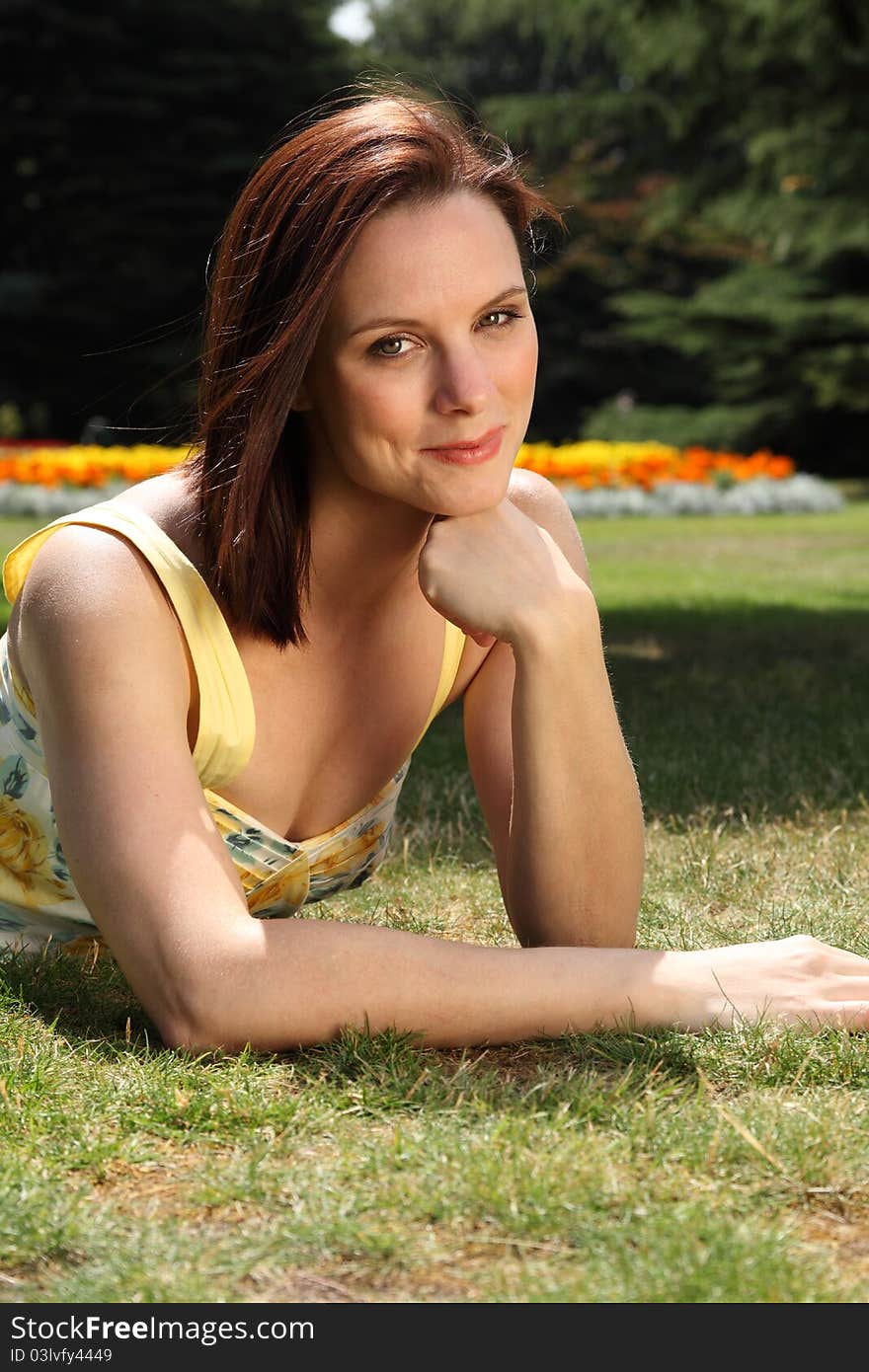 Portrait of happy smiling young woman lying on the grass in flower garden, wearing yellow summer dress and enjoying the beautiful summer sunshine. Portrait of happy smiling young woman lying on the grass in flower garden, wearing yellow summer dress and enjoying the beautiful summer sunshine.