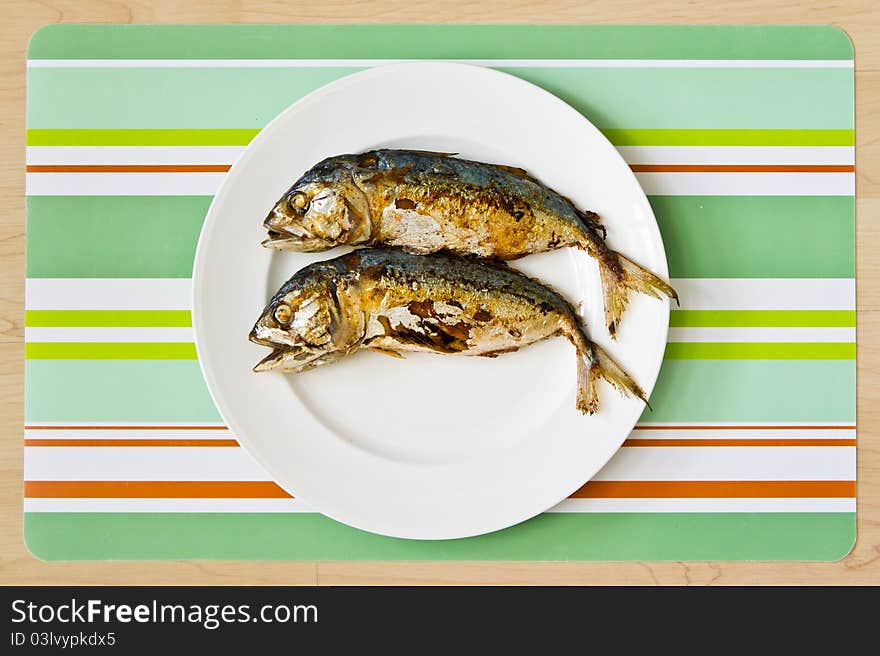 Two fried mackerel fishs on white plate