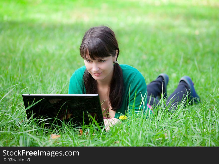 Beautiful young girl who lies with a laptop on a green lawn. Beautiful young girl who lies with a laptop on a green lawn