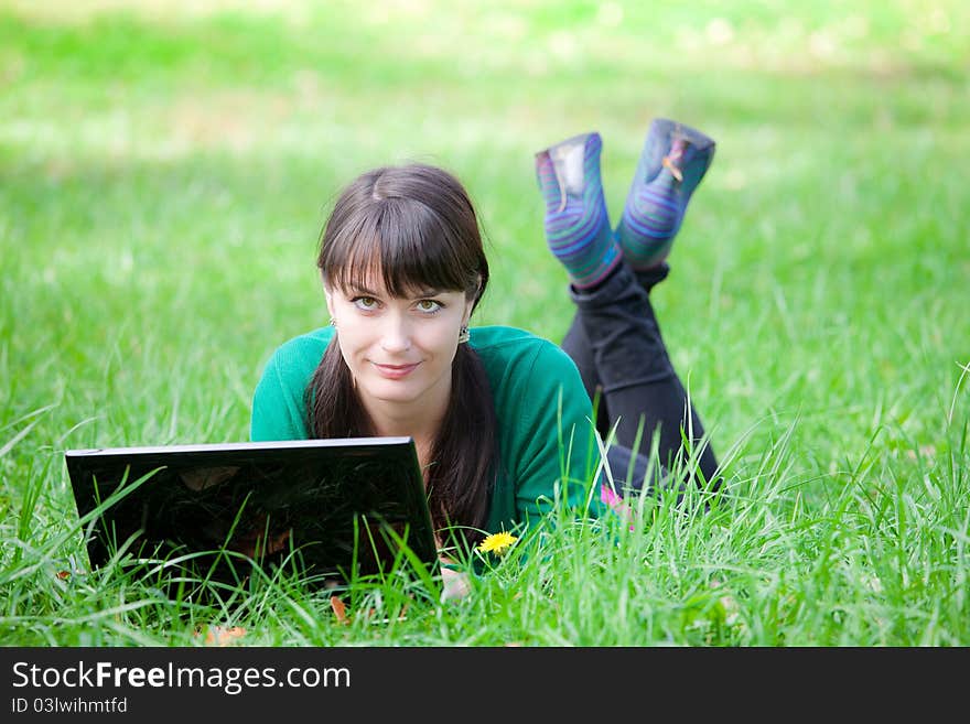 Beautiful young girl who lies with a laptop on a green lawn. Beautiful young girl who lies with a laptop on a green lawn