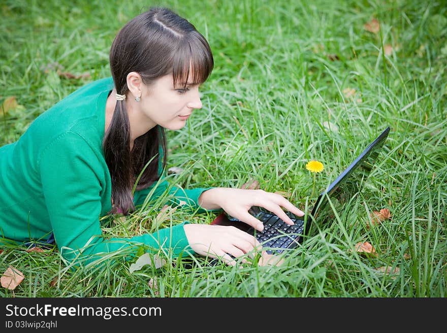 Beautiful young girl who lies with a laptop on a green lawn. Beautiful young girl who lies with a laptop on a green lawn