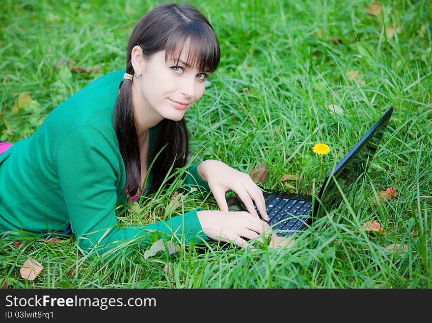 Beautiful young girl who lies with a laptop on a green lawn. Beautiful young girl who lies with a laptop on a green lawn