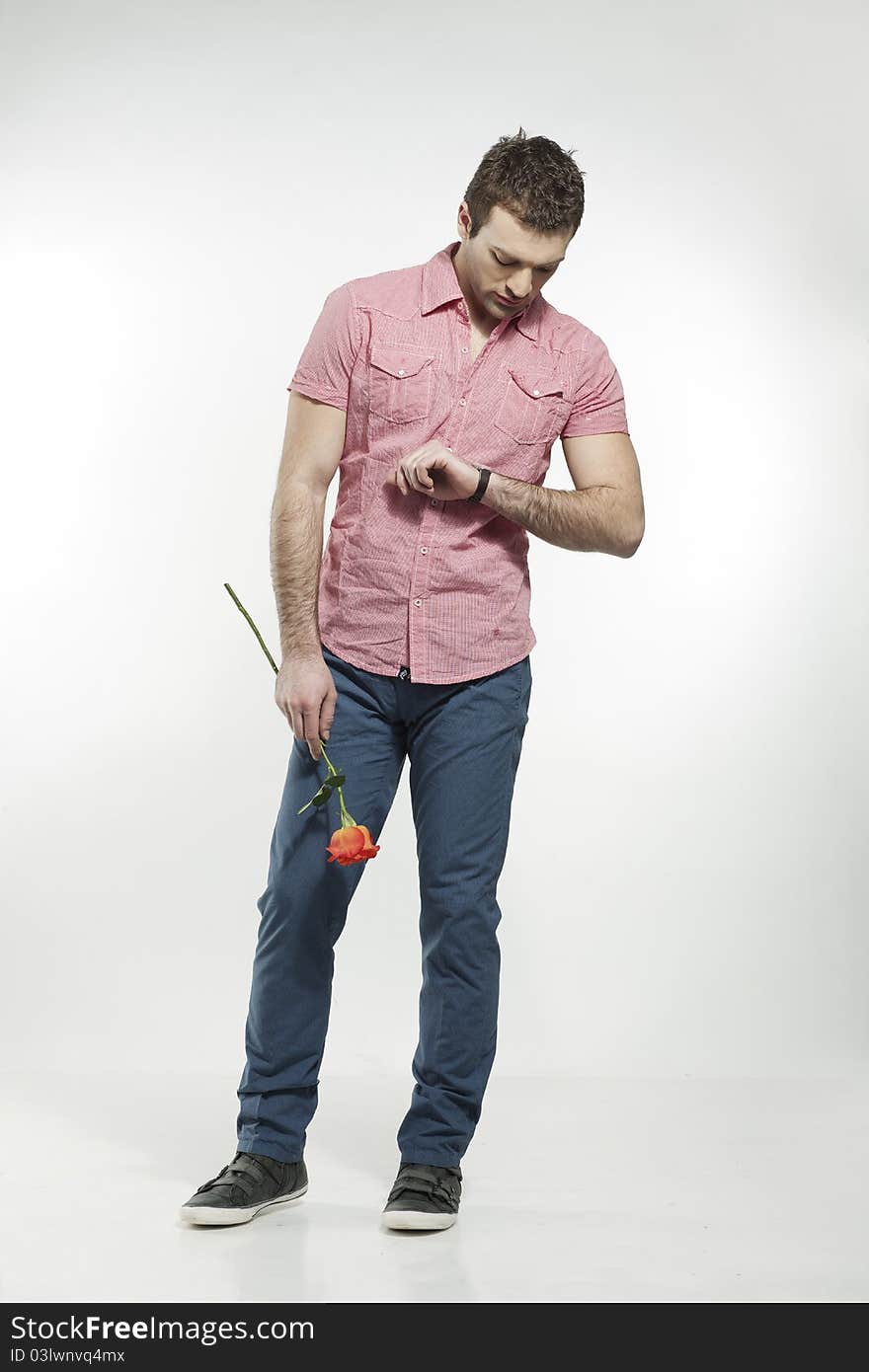 Disappointed young man waiting for his date holding a rose checking his watch. Disappointed young man waiting for his date holding a rose checking his watch