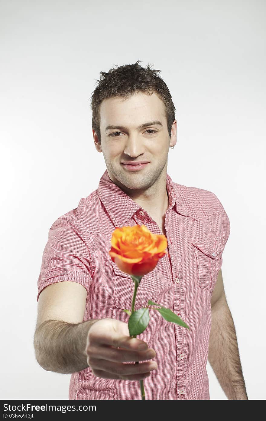 Handsome smiling young man extending his arm holding a rose. Handsome smiling young man extending his arm holding a rose