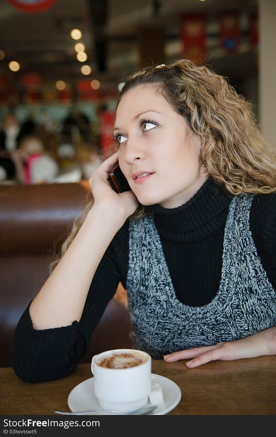 Beautiful girl with blond curly hair talking on a cell phone in cafe. Beautiful girl with blond curly hair talking on a cell phone in cafe