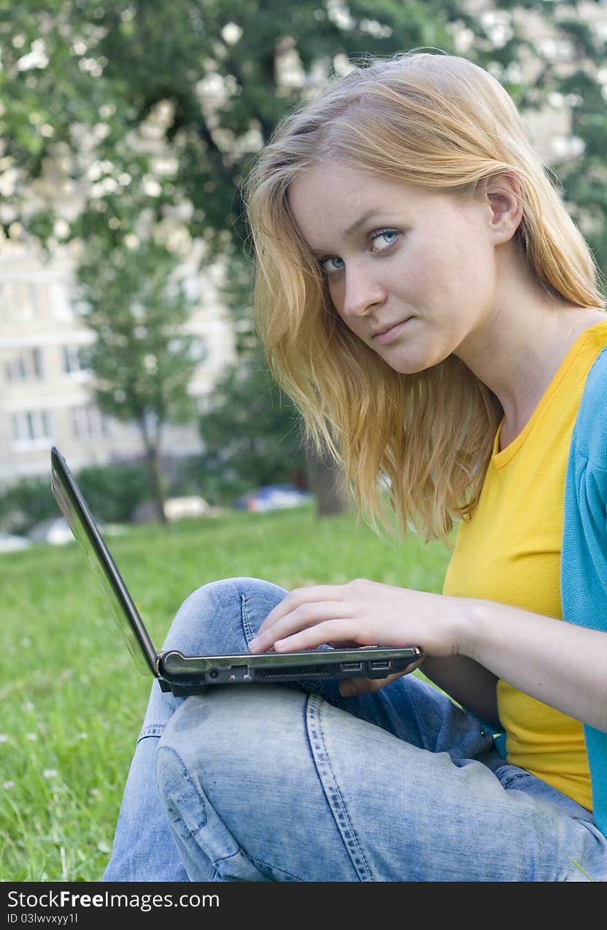 Portrait of pretty woman with laptop on the green grass