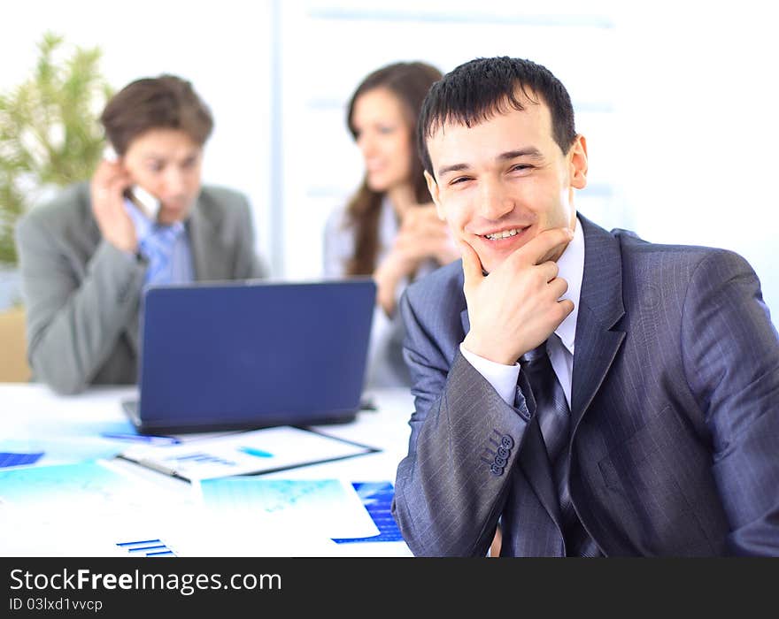 Smiling satisfied businessman looking at camera with his colleagues in the background during a meeting in the office