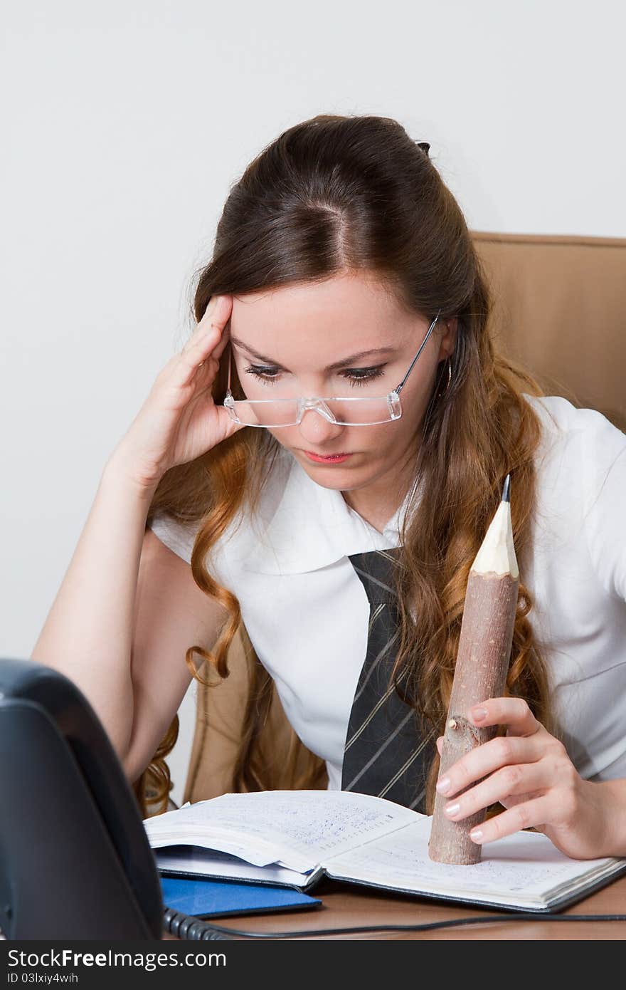 Secretary in glasses with long hair at the table looking at a notebook in the office. Secretary in glasses with long hair at the table looking at a notebook in the office