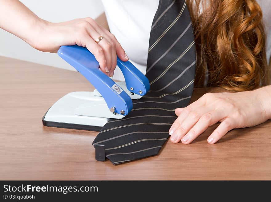 Girl breaks tie stapled to the desktop in the office. Girl breaks tie stapled to the desktop in the office