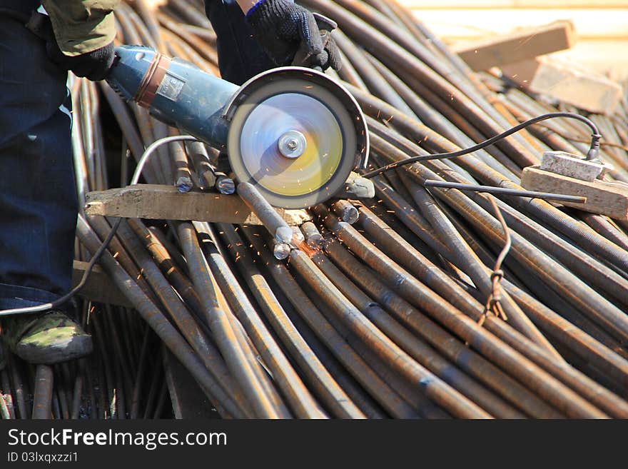 Construction worker cuts rebar circular saw on site.