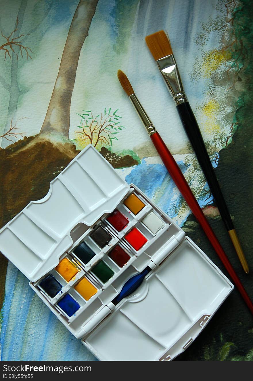 A box of watercolour paints and brushes displayed on a watercolour painting. A box of watercolour paints and brushes displayed on a watercolour painting