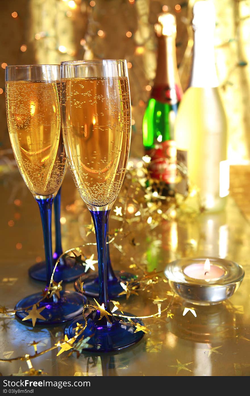 Close-up of champagne in glasses,candle light, bottles and twinkle lights on gold background.