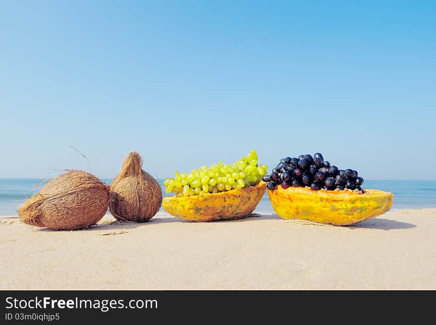 Papaya, coconut, nut and grapes on the sandy beach. Papaya, coconut, nut and grapes on the sandy beach