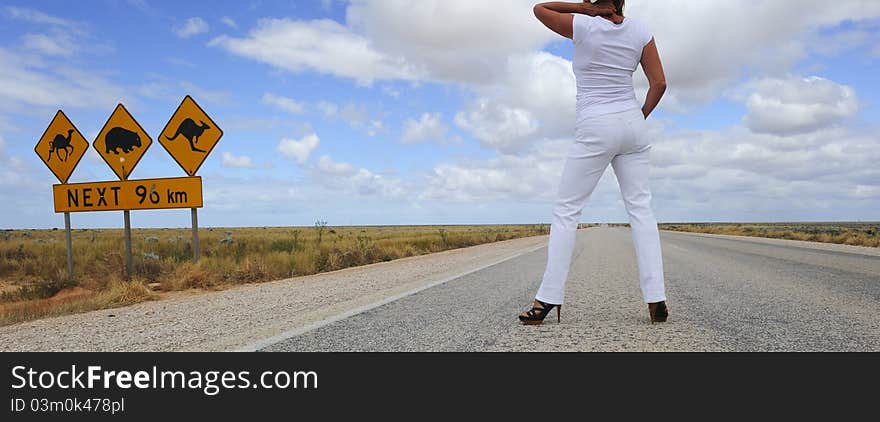 Attractive Woman standing beside famous Australian street sign in the middle of an endless highway, wearing high heel shoes. Attractive Woman standing beside famous Australian street sign in the middle of an endless highway, wearing high heel shoes.