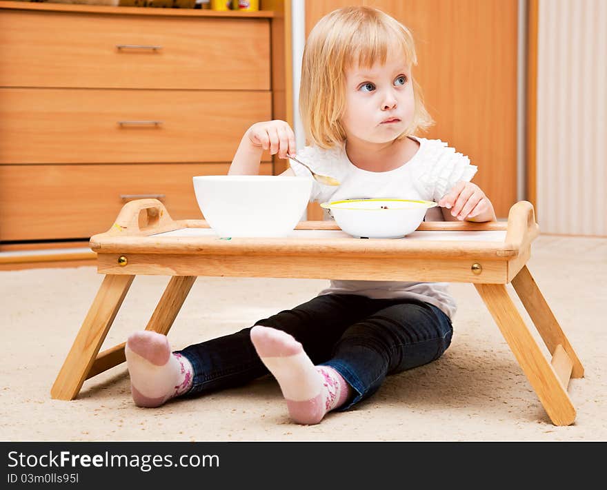 A small girl is sitting on the floor and is eating. A small girl is sitting on the floor and is eating