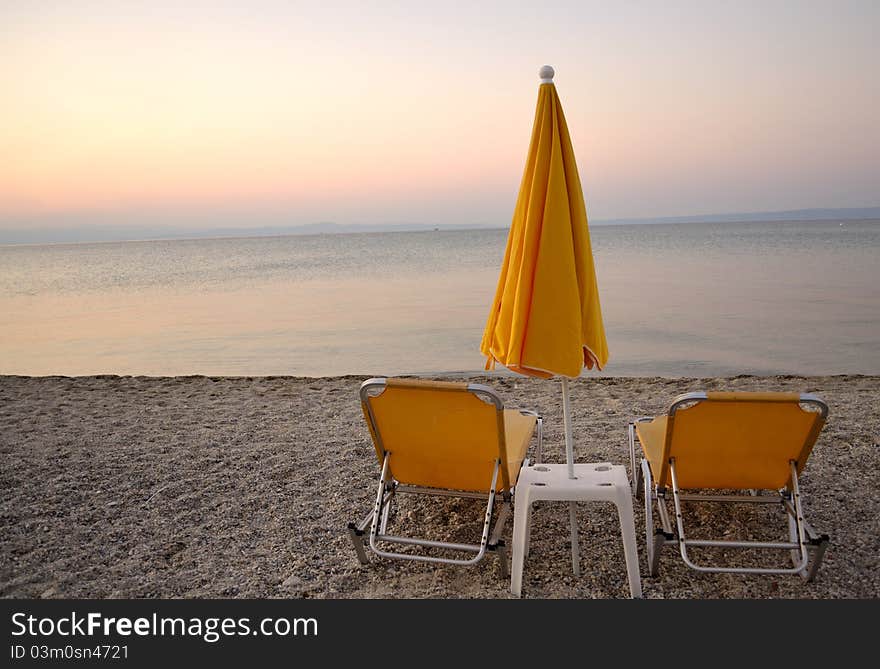 Closed umbrella on sunset with two chairs