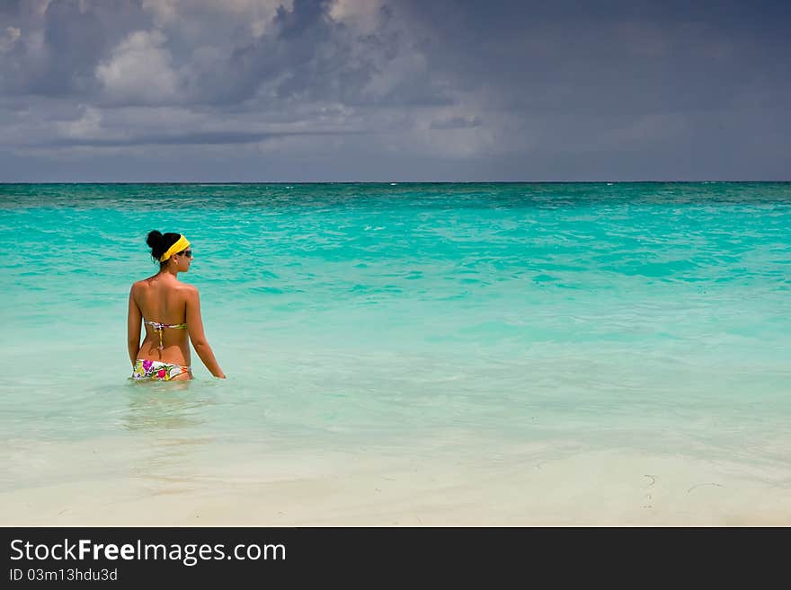 Tanned girls is standing in bright blue ocean under blue sky