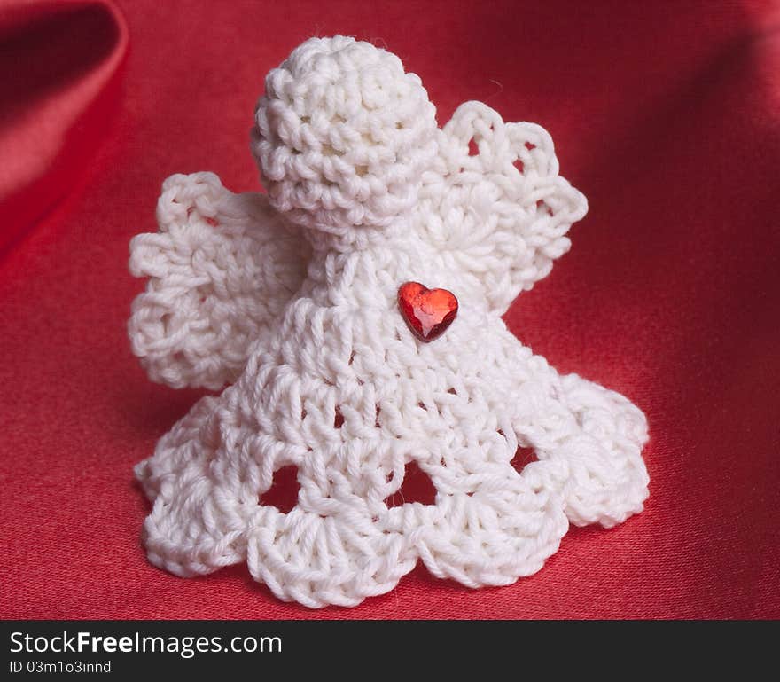 Handmade crochet Angel with a red heart on red satin background