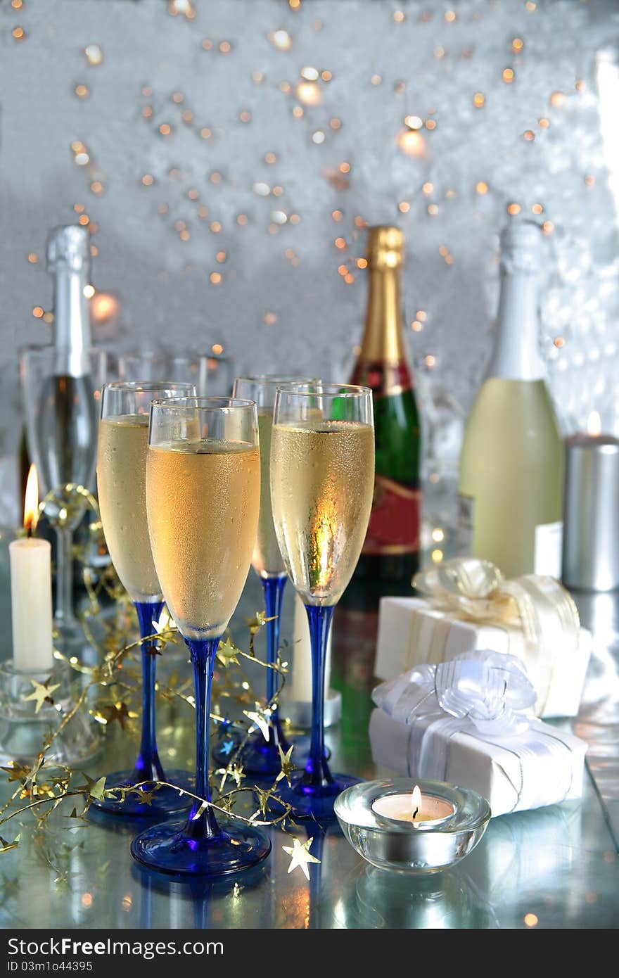 Champagne in glasses,bottles,gift boxes,candle lights and twinklelights on silver background. Champagne in glasses,bottles,gift boxes,candle lights and twinklelights on silver background.