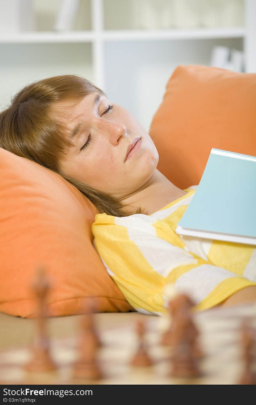 Sleeping woman with book on sofa and chess board in foreground. Sleeping woman with book on sofa and chess board in foreground