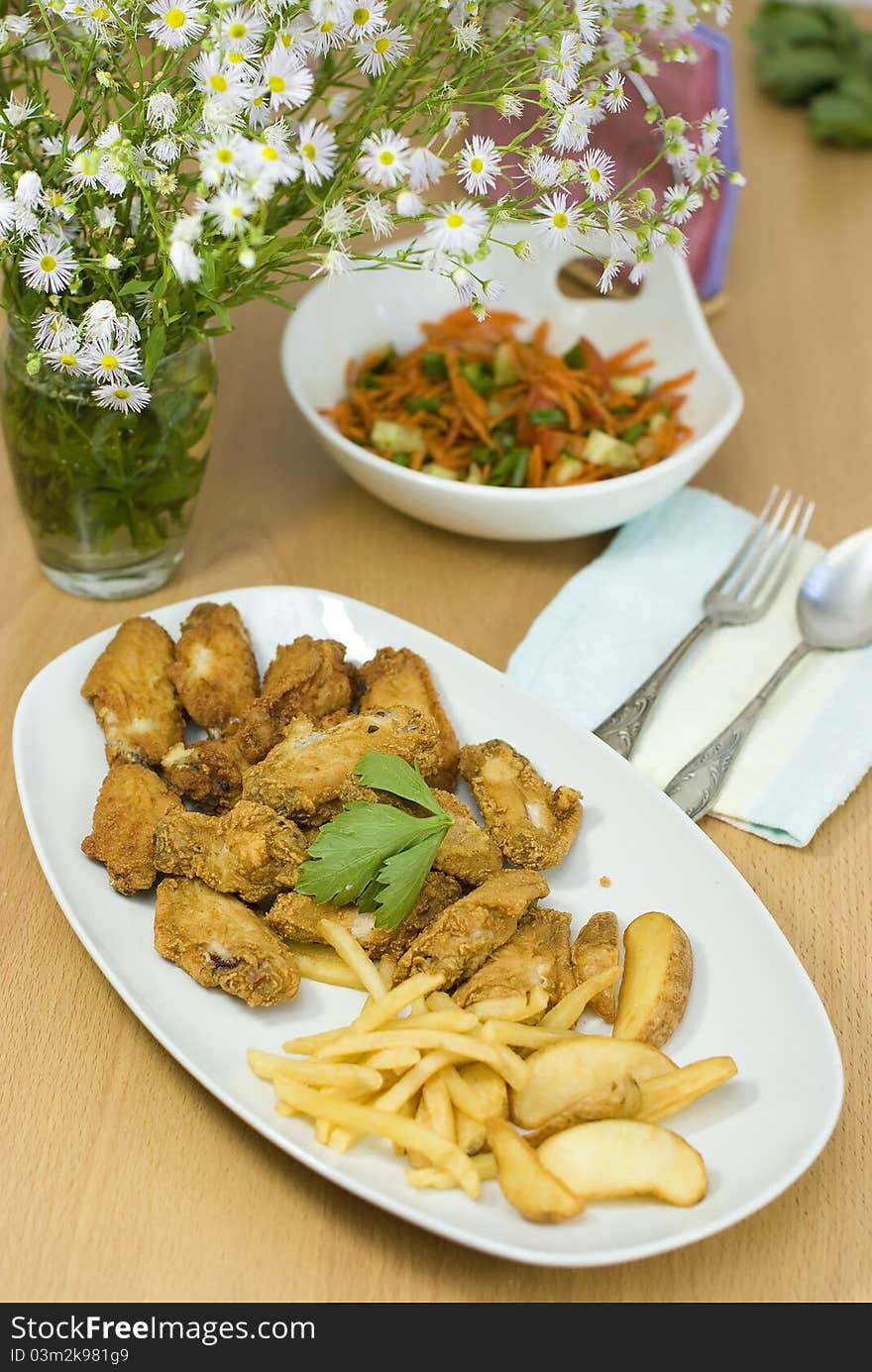 Golden fried chicken and fried potatoes in a white plate on the table