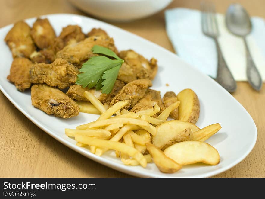 Golden fried chicken and fried potatoes in a white plate on the table