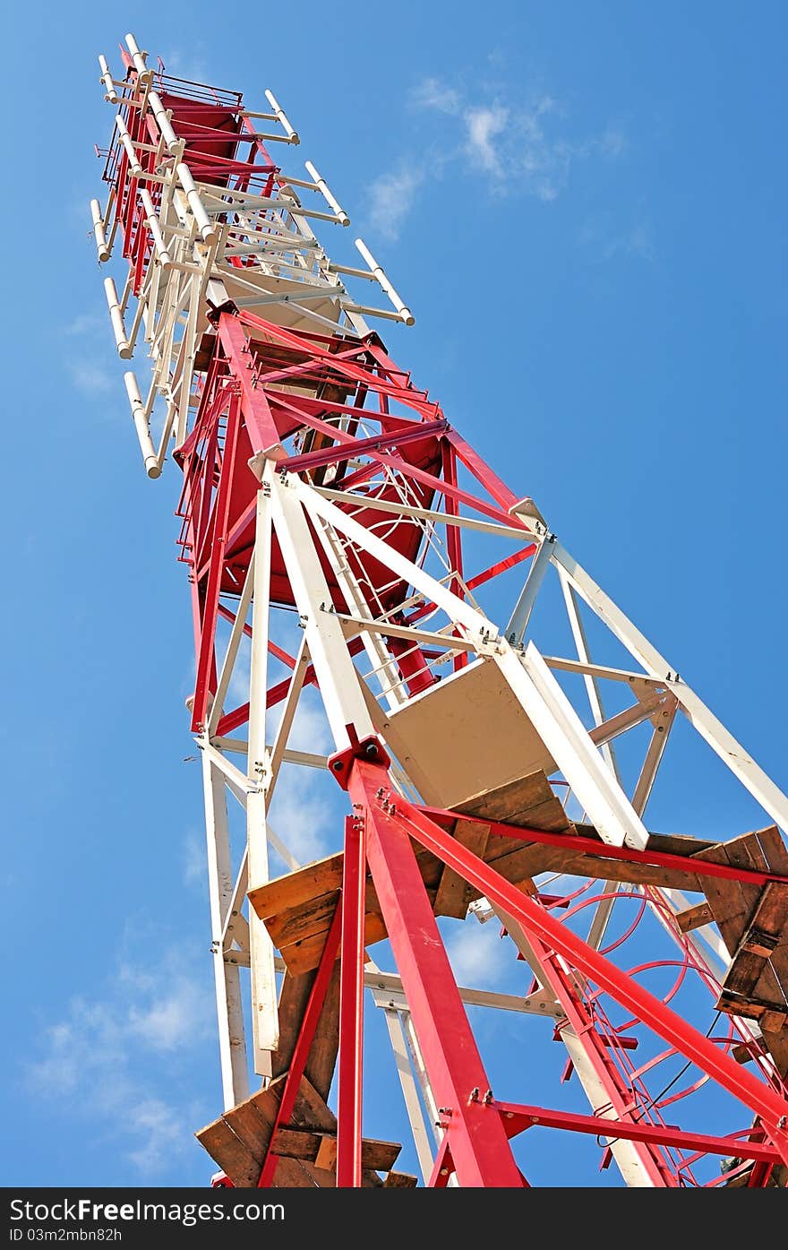 Transmitting cellular tower. GSM transmitter. Communications tower. Red tower against the blue sky. Transmitting cellular tower. GSM transmitter. Communications tower. Red tower against the blue sky.