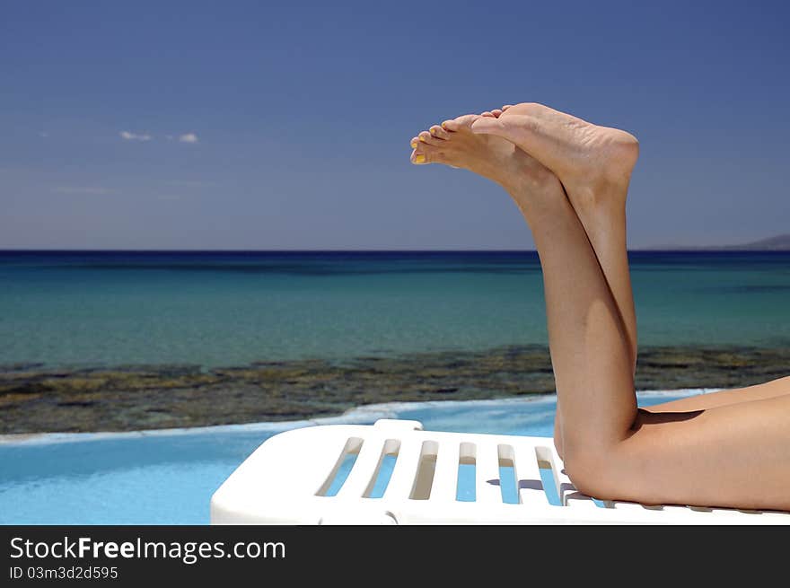 Picture of female legs over swimming pool and sea in the background. Picture of female legs over swimming pool and sea in the background