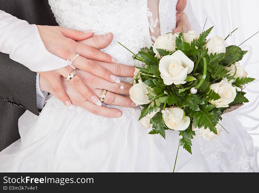 Bride and groom hands with wedding rings and bouquet of roses