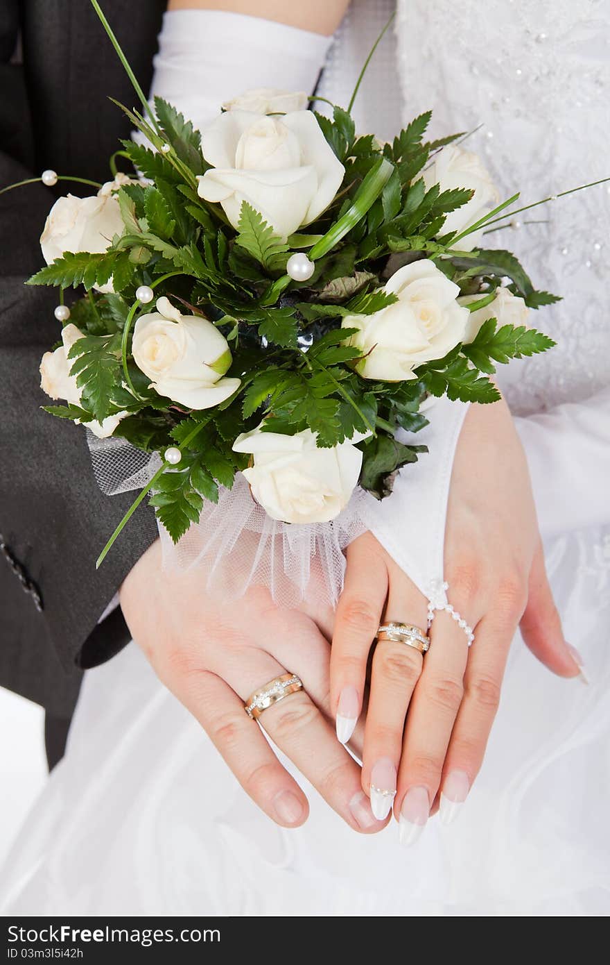 Hands of a newly-married couple with rings with a bouquet of the bride from white roses. Hands of a newly-married couple with rings with a bouquet of the bride from white roses