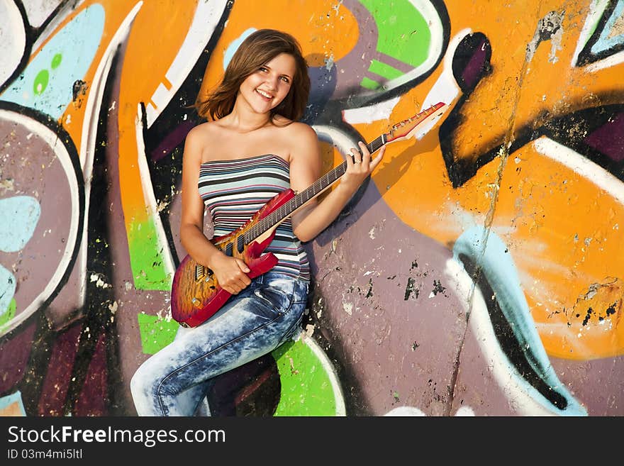 Beautiful brunette girl with guitar and graffiti wall at background.