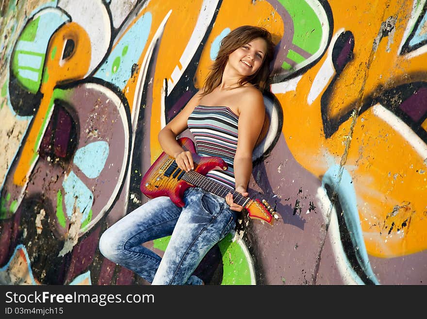 Beautiful brunette girl with guitar and graffiti wall at background.