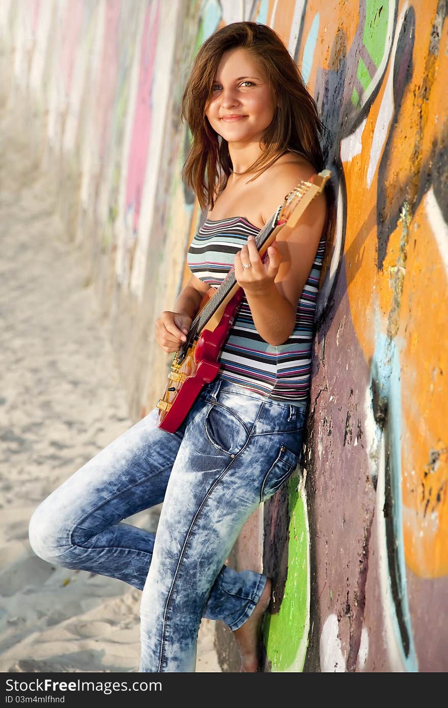 Beautiful brunette girl with guitar and graffiti wall at background.