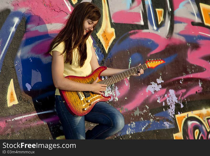 Beautiful brunette girl with guitar and graffiti wall at background.