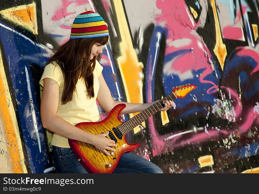 Beautiful brunette girl with guitar and graffiti wall at background.