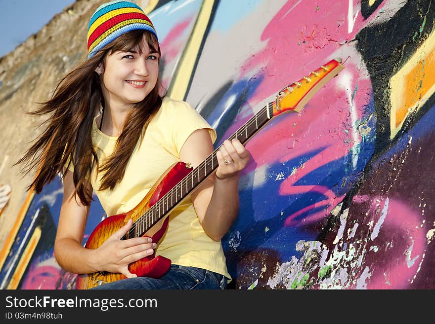 Beautiful brunette girl with guitar and graffiti wall at background.