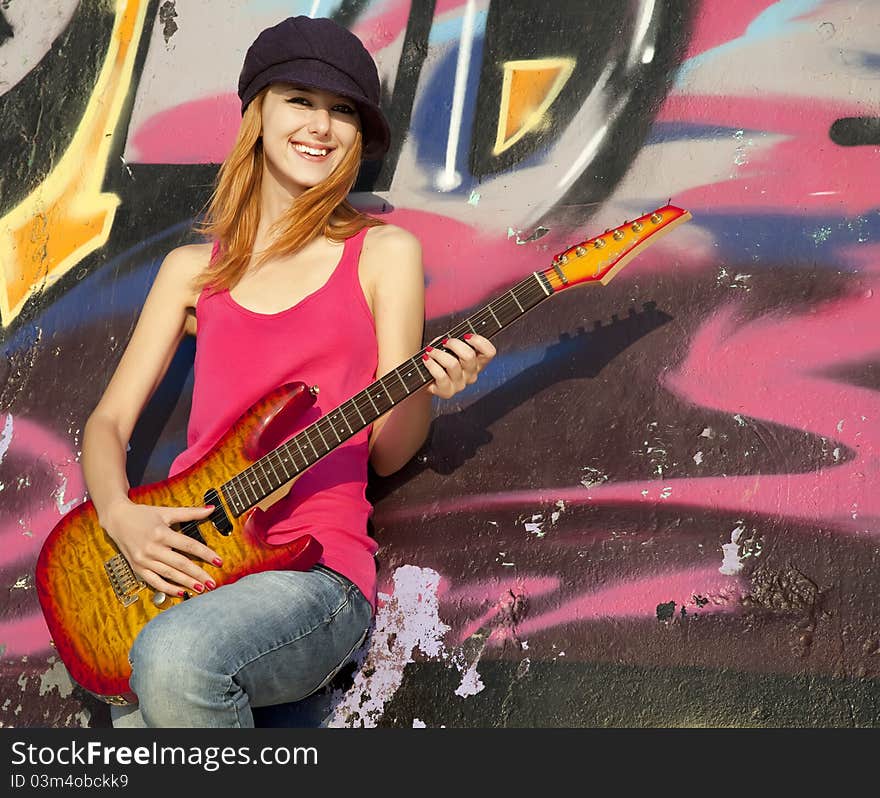 Beautiful red-haired girl with guitar and graffiti wall at background.