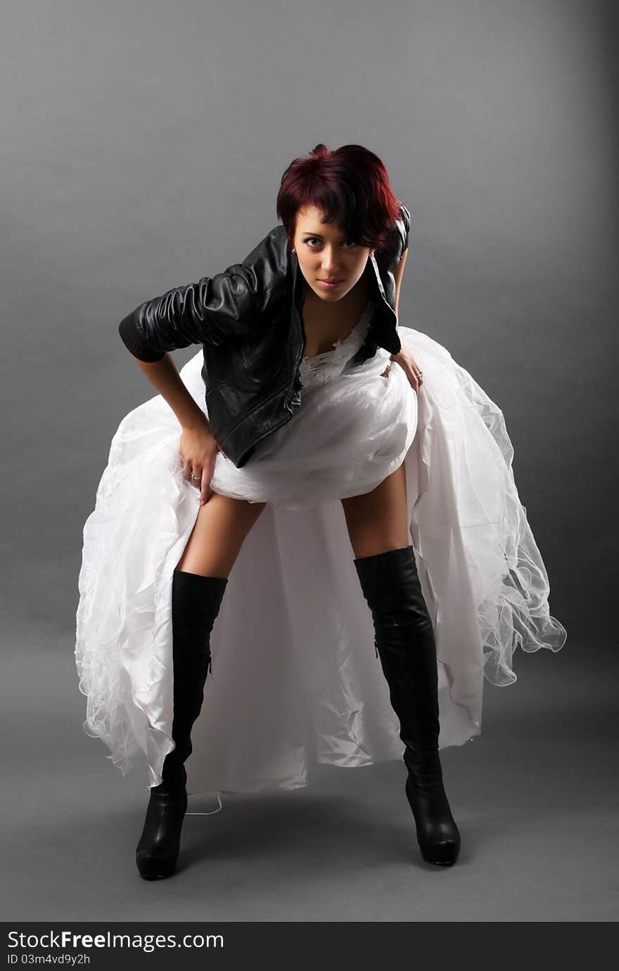 Punk bride in a white dress and a black leather jacket with a gray background