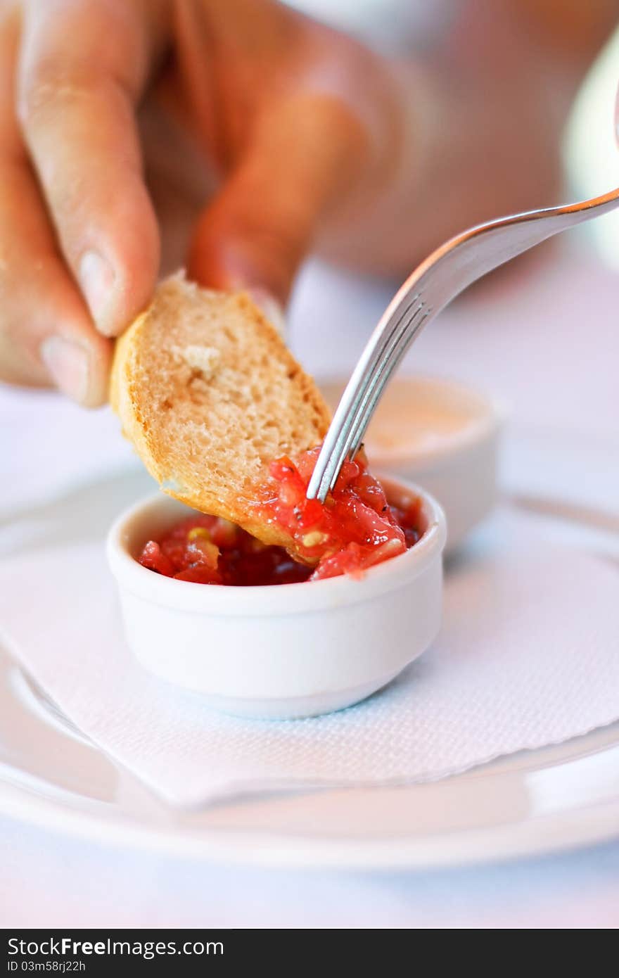 A picture of a red sauce in a small pot and a hand soping white bread into the sauce.